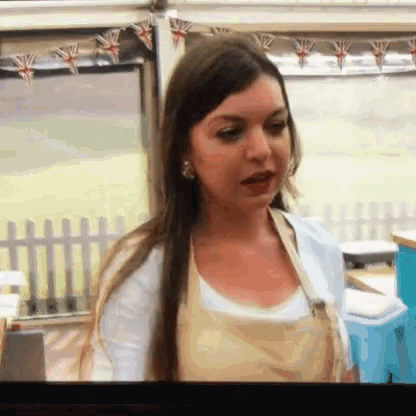 a woman wearing an apron is standing in front of a window and a fence .