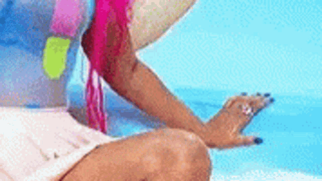 a woman with pink hair is sitting on a beach next to a pool .