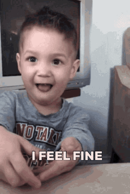 a little boy wearing a shirt that says " no tak " is smiling and saying " i feel fine "