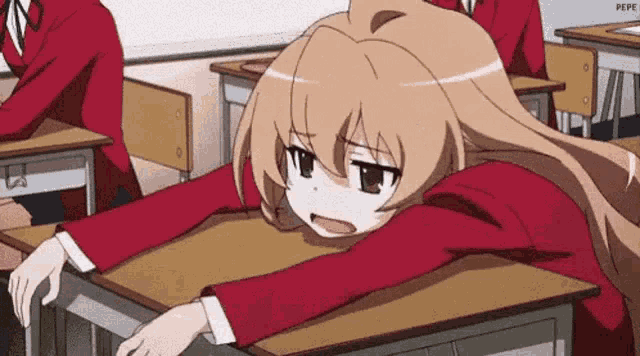 a girl is laying on a desk in a classroom with her head on it .