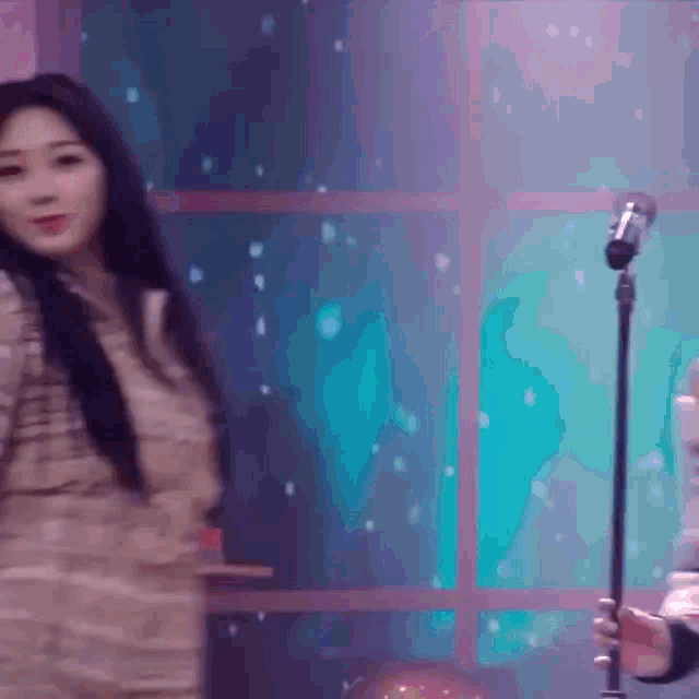 a woman is singing into a microphone while a man holds a guitar
