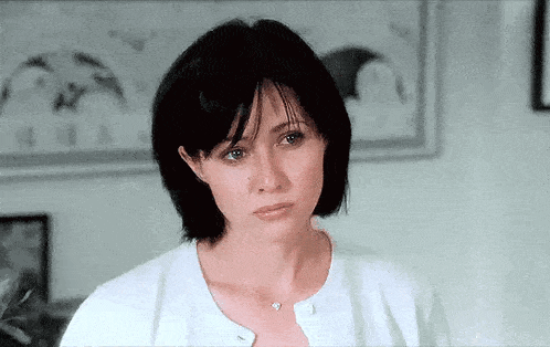 a woman with short black hair is wearing a white cardigan and necklace .