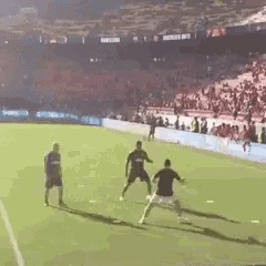 a group of men are playing soccer on a field with a crowd in the background .