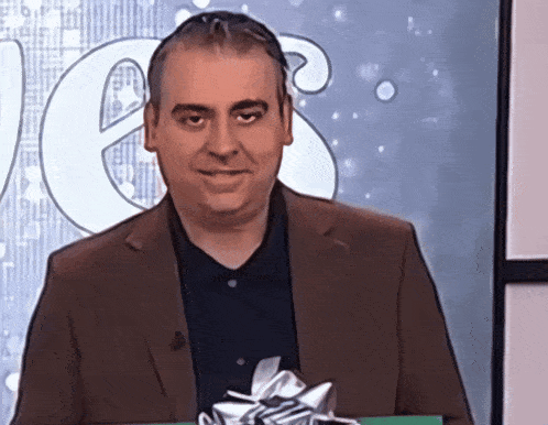 a man in a suit and black shirt holds a gift
