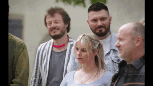 a group of people are standing in a line and one of them has a pink necklace around his neck
