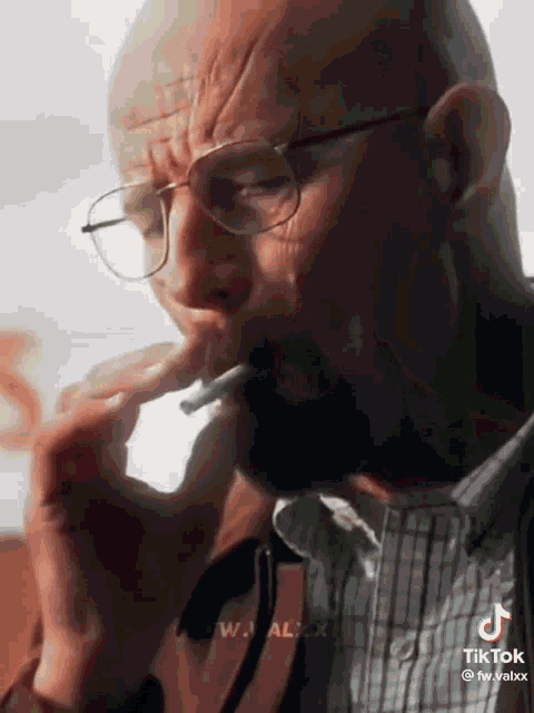 a bald man wearing glasses is smoking a cigarette .
