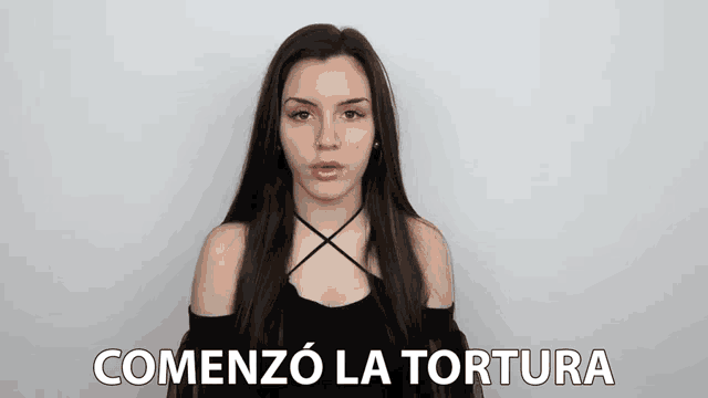 a woman with long hair is standing in front of a white wall with the words comenzo la tortura written on it .