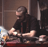 a man with a beard is sitting at a table with cards and a bottle