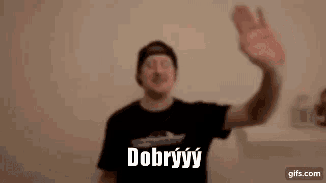 a man in a black t-shirt is waving his hand in front of a wall and says dobrýy .