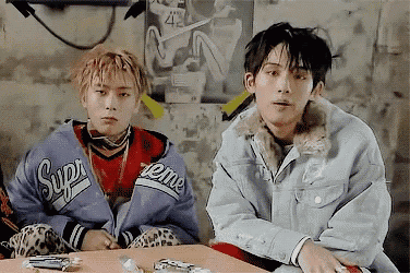 two young men are sitting at a table with one wearing a jacket that says supreme