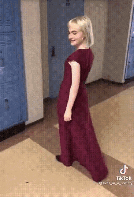 a woman in a red dress is walking down a hallway with blue lockers behind her