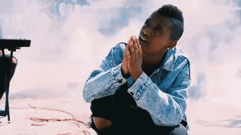 a man in a denim jacket is kneeling down with his hands folded in prayer .