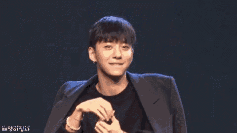 a young man in a suit is sitting at a table with his hands on his face .