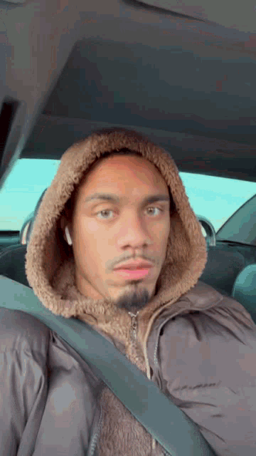 a man wearing a hooded jacket and a seat belt is sitting in a car