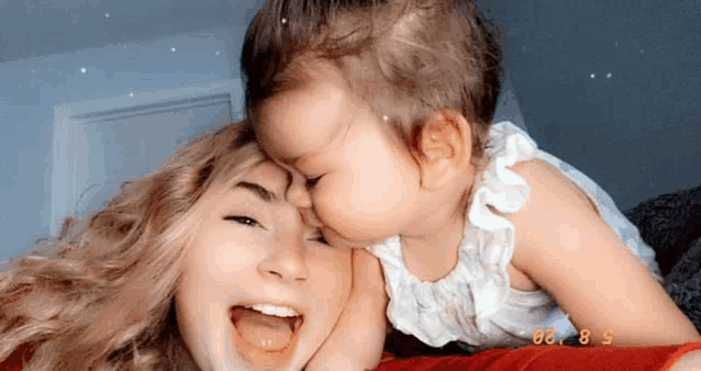 a little girl is kissing a woman on the cheek while laying on a bed .