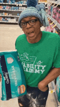 a woman wearing a green shirt that says ability academy holds a package of underwear