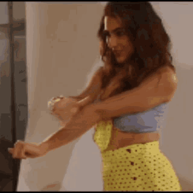 a woman in a blue crop top and yellow polka dot skirt is standing in front of a window .
