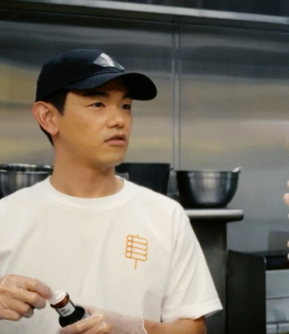 a man wearing a white shirt and a black hat holds a bottle of liquid