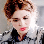 a woman wearing a denim jacket and a braided hairstyle is looking down .