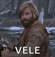 a man with a beard and long hair is standing in front of a sign that says vele