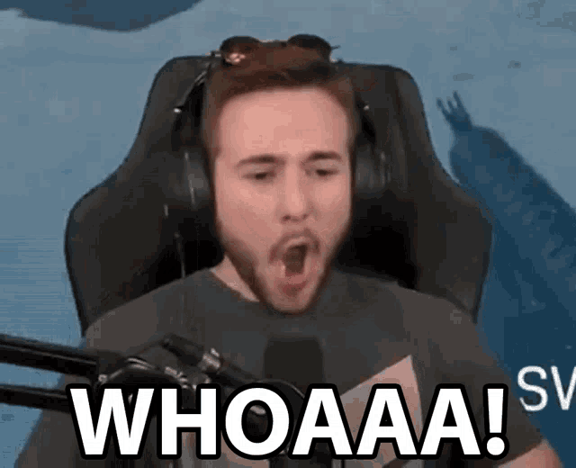 a man wearing headphones is sitting in front of a microphone and making a funny face with his mouth open .