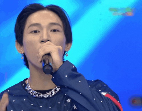 a young man singing into a microphone with a blue background behind him