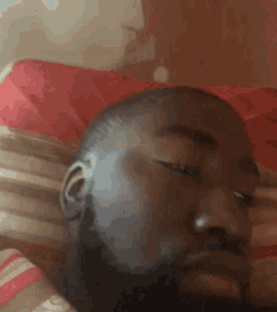 a man with a beard is laying in bed with his eyes closed and a red pillow .
