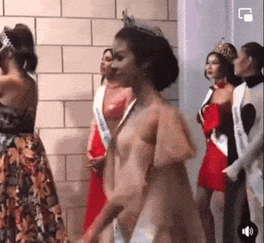 a group of women in dresses are standing next to each other in front of a brick wall .