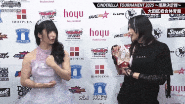 two women are standing in front of a wall that says hoyu on it