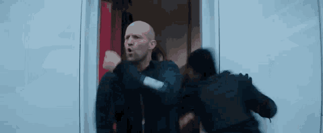 a man is standing in a doorway with his fist in the air and a woman is running behind him .