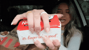 a woman in a car is holding a box that says " it 's finger lick good "