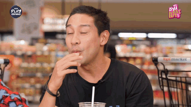 a man in a black shirt is drinking from a plastic cup with a straw in a store