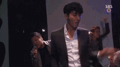 a man in a suit is singing into a microphone while dancing in front of a sbs logo .