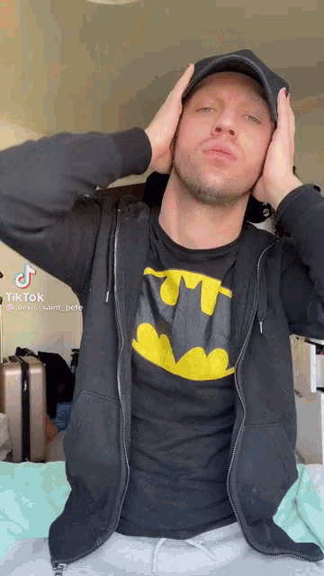 a man wearing a black jacket and a batman t-shirt is covering his ears with his hands