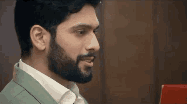 a man with a beard is wearing a green jacket and a white shirt