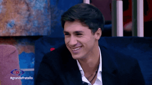 a man in a suit is smiling in front of a sign that says grande fratello