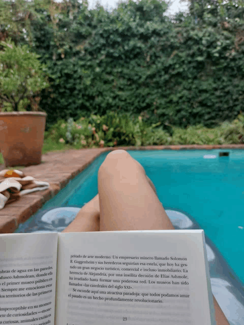 a book is open to page 23 and a person is laying in a pool with their legs crossed