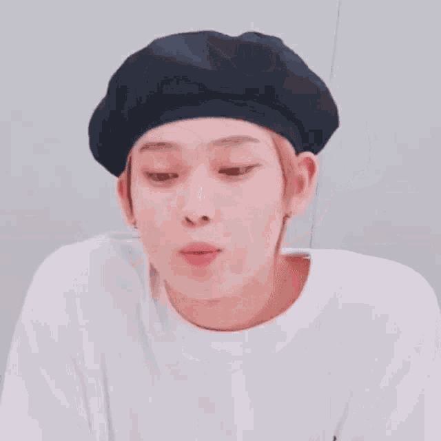 a young man wearing a black beret and a white shirt is making a funny face .