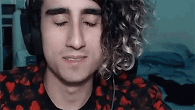 a young man with curly hair is wearing headphones and looking down .