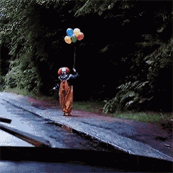 a clown is holding a bunch of balloons on the side of the road