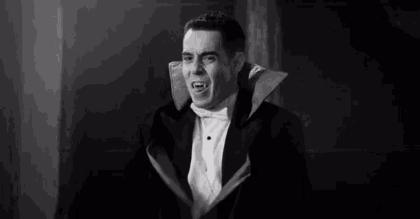 a man in a tuxedo and bow tie is dressed as a vampire with his mouth open .