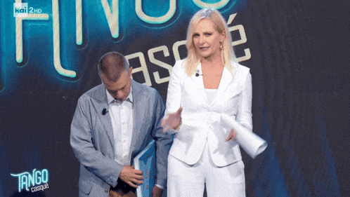a woman in a white suit stands next to a man in a blue suit in front of a sign that says tango