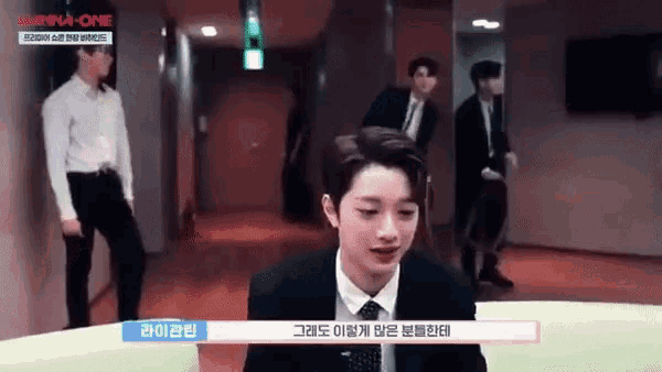 a man in a suit and tie is sitting at a table in a hallway with other people .