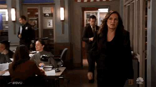 a woman in a black dress walks through a hallway with nbc written on the bottom right