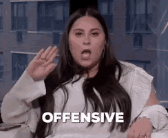 a woman is sitting on a couch with her mouth open and making a funny face while saying `` offensive '' .