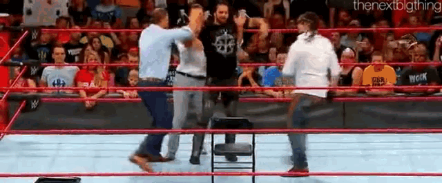 a group of men are standing in a wrestling ring with a chair in the middle .