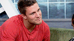 a man in a red shirt is sitting on a couch looking at something .