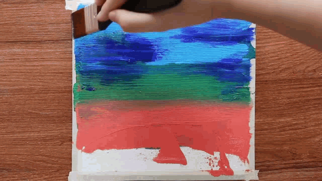 a person is painting a painting with a brush on a wooden table .