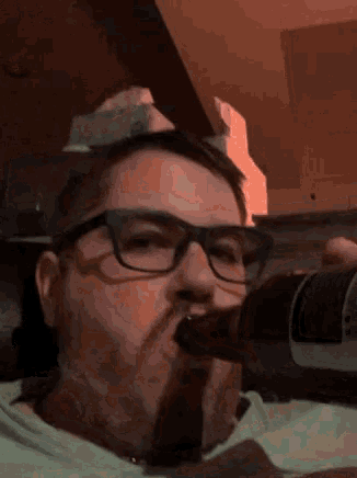 a man wearing glasses is drinking a bottle of coke