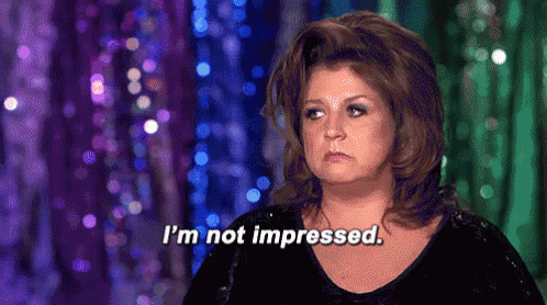 a woman says i 'm not impressed while standing in front of a purple curtain .